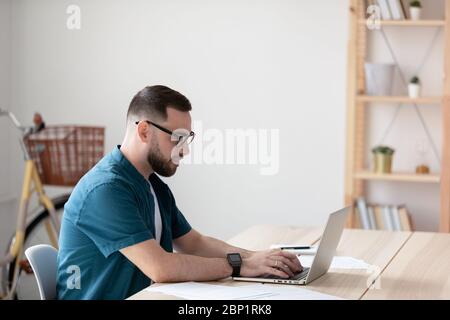 Vue latérale beau jeune homme d'affaires tapant sur le clavier à l'aide d'un ordinateur portable. Banque D'Images
