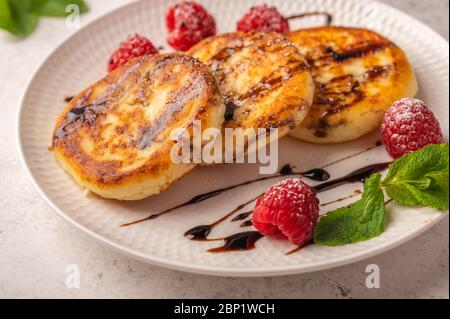 Cheesecakes maison aux framboises, sirop et menthe sur une plaque en céramique sur fond de bois clair. Gros plan. Copier l'espace pour le texte Banque D'Images