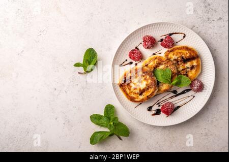 Cheesecakes maison aux framboises, sirop et menthe sur une plaque en céramique sur fond de bois clair. Vue de dessus. Copier l'espace pour le texte Banque D'Images