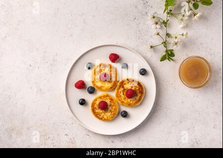 Cheesecake russe traditionnel avec framboises, bleuets et miel sur une plaque en céramique blanche sur fond clair. À côté de lui est une branche de floraison Banque D'Images