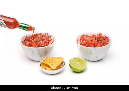 2 bols identiques contenant de la salsa fraîchement préparée avec une bouteille de sauce tabasco versée dans un bol, avec un bol de chips tortilla et un demi-bol Banque D'Images