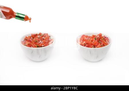 2 bols identiques contenant de la salsa fraîchement préparée avec une bouteille de sauce tabasco versée dans un bol Banque D'Images