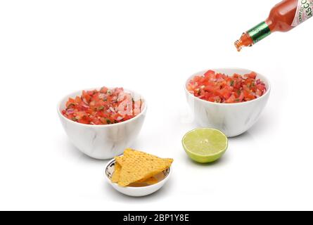 2 bols identiques contenant de la salsa fraîchement préparée avec une bouteille de sauce tabasco versée dans un bol, avec un bol de chips tortilla et un demi-bol Banque D'Images