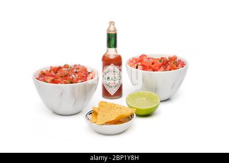 2 bols identiques contenant de la salsa fraîchement préparée avec une bouteille de sauce tabasco, un bol de chips tortilla et une demi-tranche de lime fraîche Banque D'Images