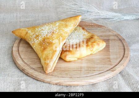 samsa, carré asiatique et triangulaire, aux graines de sésame feuilletées sur un plateau de cuisine en bois sur fond de toile de fond Banque D'Images