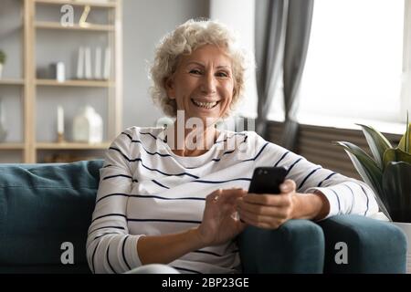 Souriante positive femme d'âge moyen tenant le smartphone entre les mains. Banque D'Images