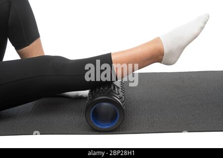 Une femme d'âge moyen sur un rouleau myofascial fait un massage de jambe de shin sur un fond blanc. Banque D'Images