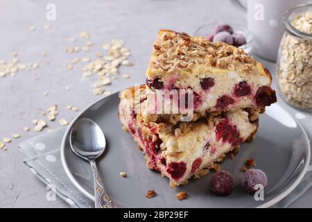 Tranches de cocotte de fromage maison avec flocons d'avoine et cerise sur une plaque grise sur fond de béton gris, gros plan, format horizontal Banque D'Images