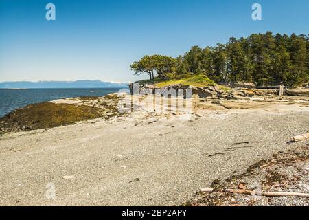 À marée basse, un petit îlot a séché pour révéler une plage de galets, avec vue sur le détroit de Georgia et les montagnes sur le continent de la Colombie-Britannique. Banque D'Images