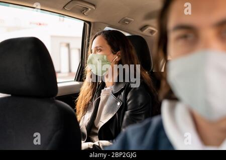 Jeune femme avec écouteurs et masque de protection regardant par la fenêtre tout en étant assise sur le siège arrière de la voiture et en allant à la maison en taxi Banque D'Images