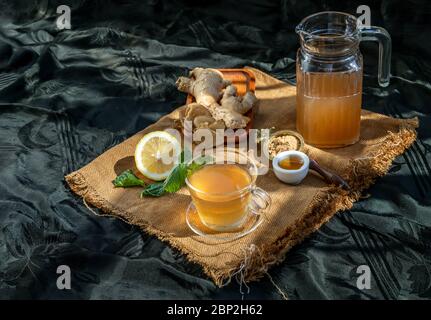 Jus de gingembre chaud avec citron et menthe, racine et tranches de gingembre servies avec du sucre brun et du miel sur fond de tissu de sac. Le jus de gingembre chaud peut aider Banque D'Images