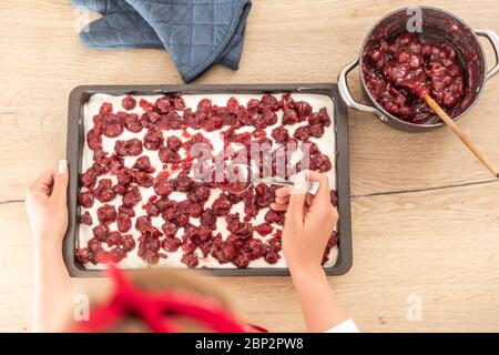 Vue de dessus d'une femme mettant des cerises cuites sur une glace de glaçage d'un gâteau avec une cuillère. Banque D'Images