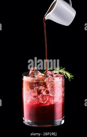 Verser l'espresso dans un tonique avec du jus de cerise isolé sur fond noir Banque D'Images