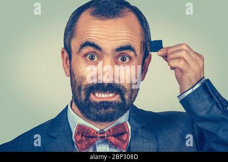 Concept de mémoire externe nécessaire. Portrait d'un homme d'affaires à barbe en colère portant une veste élégante et un noeud papillon rouge tenant une carte micro SD près de sa tête isola Banque D'Images