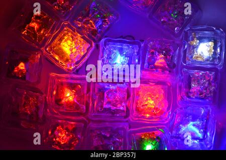 De nombreuses couleurs différentes de petits cubes de glace lumineux en plastique flottant dans l'eau sont situées dans des plats en argile ukrainienne. Banque D'Images