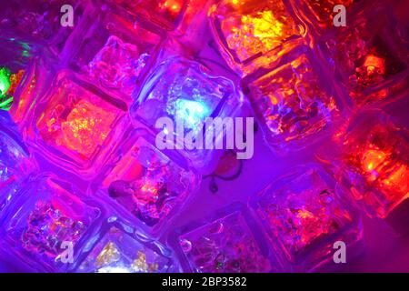 De nombreuses couleurs différentes de petits cubes de glace lumineux en plastique flottant dans l'eau sont situées dans des plats en argile ukrainienne. Banque D'Images