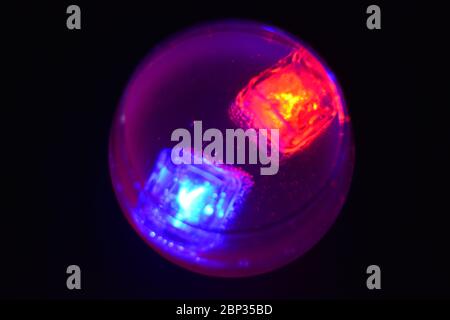 Les glaçons rouges et bleus brillants qui flottent dans une délicieuse boisson froide blanche dépolie sont placés dans un verre cognac sur un fond noir dépoli. Banque D'Images