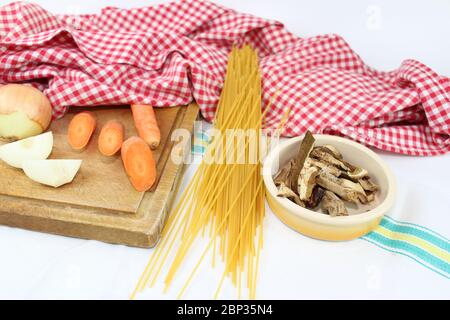 Produits alimentaires disposés sur la table à volants, avec des carrés rouges et blancs. Cuisine méditerranéenne italienne avec spaghetti et champignons porcini séchés. Banque D'Images