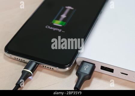 Le smartphone est chargé en gros plan depuis la batterie portable située sur l'arrière-plan de la table lumineuse. Concept de technologie moderne. Mise au point sélective. Banque D'Images
