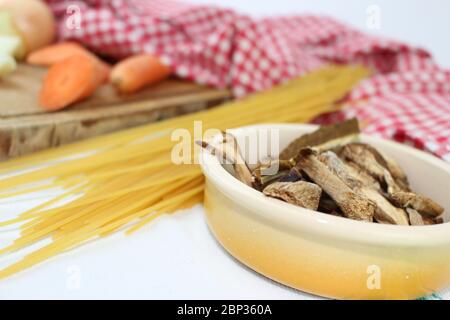 Produits alimentaires disposés sur la table à volants, avec des carrés rouges et blancs. Cuisine méditerranéenne italienne avec spaghetti et champignons porcini séchés. Banque D'Images