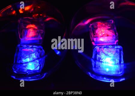 De grands verres aux différentes couleurs de glaçons lumineux avec une boisson savoureuse sont situés sur un fond noir mat. Banque D'Images