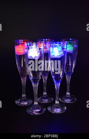 Cinq gobelets en verre sur de longues jambes torsadées avec des glaçons aux couleurs différentes. Des boissons amusantes et lumineuses avec des éléments LED lumineux sont situées. Banque D'Images