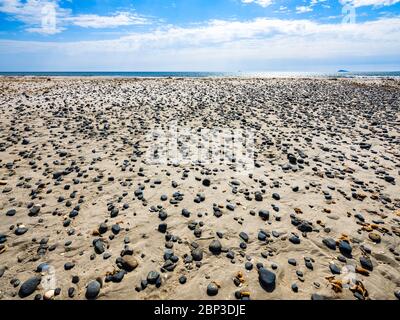 Petites pierres noires et coquillages dispersés sur le sable de la plage de Porto Pino, Sant’Anna Arresi, Sardaigne, Italie Banque D'Images