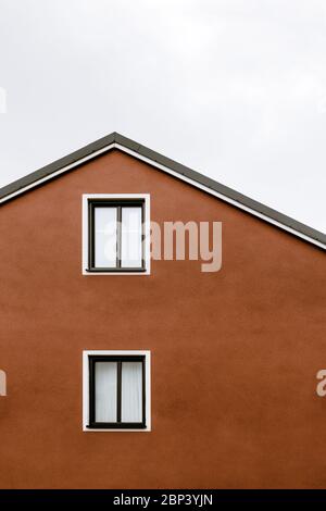 Façade et toit d'une maison orange avec fenêtres blanches, ciel nuageux. Banque D'Images