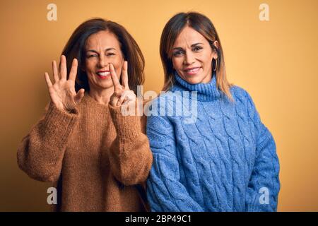 Âge moyen beau couple de sœurs portant un pull décontracté sur fond jaune isolé montrant et pointant vers le haut avec les doigts numéro sept pendant Banque D'Images