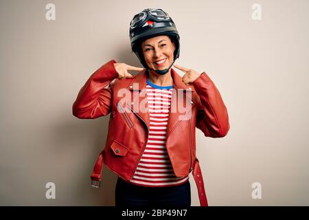 Femme motard d'âge moyen portant un casque et une veste de moto sur fond blanc souriant gai montrant et pointant avec les doigts dents et Banque D'Images