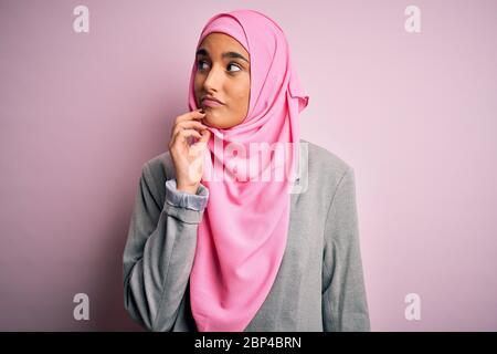 Jeune femme d'affaires brunette, vêtue de hijab musulman rose et de veste d'affaires avec main sur le menton, pensant à la question, expression pensive. SM Banque D'Images