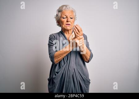 Senior belle femme à cheveux gris portant une robe décontractée debout sur fond blanc souffrant de douleur sur les mains et les doigts, arthrite inflammation Banque D'Images