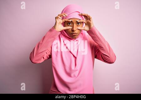 Jeune afro-américaine africaine portant le hijab musulman sur fond rose isolé essayant d'ouvrir les yeux avec les doigts, endormi et fatigué pour le matin fa Banque D'Images