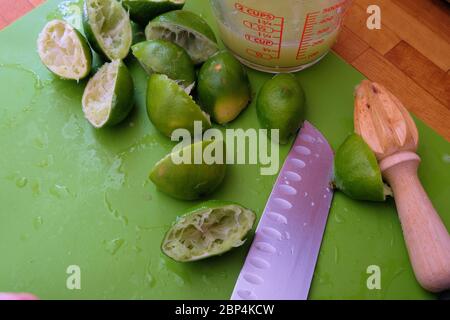 Jus de lime dans une tasse à mesurer en verre avec des limes jurées coupées en deux sur une planche à découper en bois avec un couteau et un alésoir; pressés ou alésés pour le jus. Banque D'Images