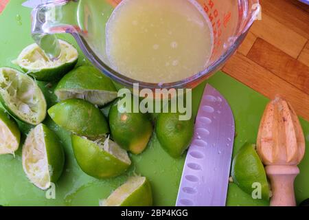 Jus de lime dans une tasse à mesurer en verre avec des limes jurées coupées en deux sur une planche à découper en bois avec un couteau et un alésoir; pressés ou alésés pour le jus. Banque D'Images