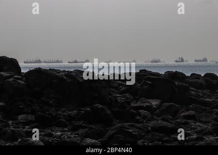 D'énormes navires se trouvant sur l'océan, alignés à l'horizon, dans une mer étincelante, attendent leur tour pour entrer dans le canal de Panama, vu d'une côte rocheuse. Copier l'espace Banque D'Images