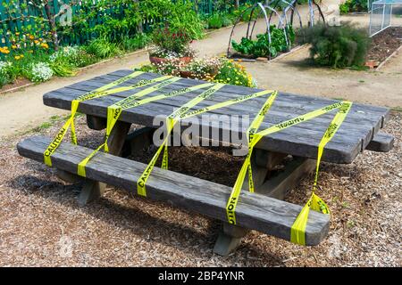 Table de pique-nique en bois dans le parc public protégée par du ruban de barricade jaune pour empêcher l'utilisation accidentelle pendant l'ordre de séjour à la maison au coronavirus, Covid-19 Banque D'Images