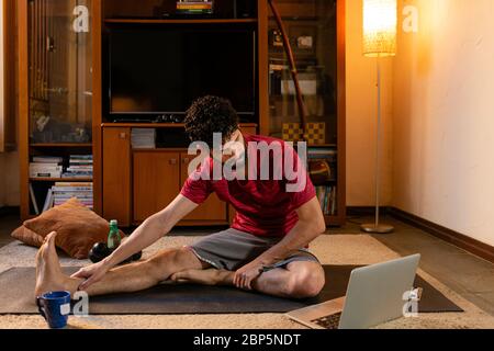 Jeune homme qui exécute l'étirement pendant la classe en ligne. Concept d'entraînement à domicile. Banque D'Images