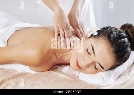 Jeune femme souriante bénéficiant d'un massage relaxant du cou et du dos au spa Banque D'Images