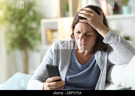 Triste femme adulte lisant de mauvaises nouvelles sur un smartphone assis sur un canapé à la maison Banque D'Images