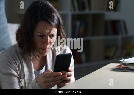 Inquiète femme adulte lisant de mauvaises nouvelles sur smartphone assis sur le sol la nuit à la maison Banque D'Images