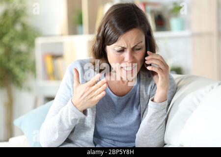 Une femme d'âge moyen en colère se disputant un appel sur un smartphone assis sur un canapé à la maison