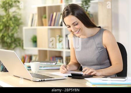 Bonne comptable femme calculant sur la calculatrice assis sur un bureau à la maison Banque D'Images