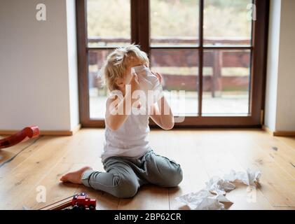 Petit garçon malade avec froid à la maison assis sur le sol, éternuant. Banque D'Images