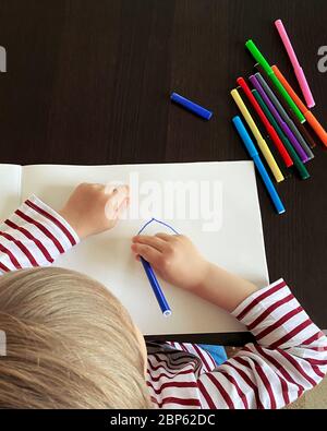 Un petit garçon tire à la table. Vue de dessus, des stylos feutre de différentes couleurs sont sur la table Banque D'Images