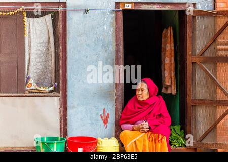 Katmandou, Népal - 24 novembre 2018 : ancienne femme népalaise regardant dehors tout en étant assise sur la porte à la maison à Katmandou. Style de vie décontracté des personnes âgées p Banque D'Images