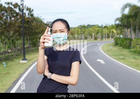 Jeune femme dans un masque de protection médicale et tenant un alcool en main. Campagne pour utiliser un masque de protection et de l'alcool pour protéger COVID19 Banque D'Images