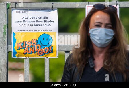 Dresde, Allemagne. 18 mai 2020. Constanze Hänsel, la maîtresse d'une école primaire, porte un garde-bouche en attendant devant un panneau disant «s'il vous plaît ne pas entrer dans le bâtiment de l'école pour amener vos enfants - Kiss an Go» pour l'arrivée des élèves. À partir de ce lundi, les écoles primaires et secondaires ouvriront à nouveau leurs portes après des semaines de fermeture forcée en raison de la pandémie de Corona. Crédit : Robert Michael/dpa-Zentralbild/dpa/Alay Live News Banque D'Images