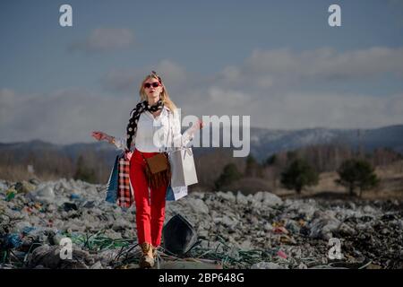 Femme avec des sacs de shopping sur la décharge, consumérisme contre pollution concept. Banque D'Images