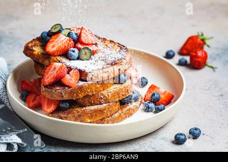 Toast traditionnel français avec bleuets, fraises et sucre en poudre sur une assiette blanche. Banque D'Images